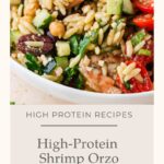 A bowl of Shrimp Orzo Salad with cucumbers, tomatoes, olives, chickpeas, and herbs, labeled as a high-protein recipe called High-Protein Shrimp Orzo Salad.