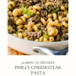 A skillet filled with Philly Cheesesteak Pasta—tender pasta tossed with sliced beef, green bell peppers, and melted cheese—captures all the classic flavors of the iconic sandwich in a hearty weeknight meal. Text below reads 30 Minute Dinners: Philly Cheesesteak Pasta.