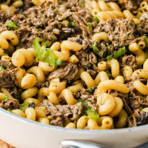 A close-up of a skillet filled with cooked cavatappi pasta, pieces of beef, mushrooms, and chopped green peppers in a creamy sauce.